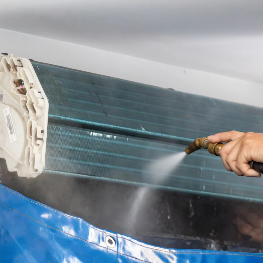 Technician using a spray nozzle to clean an air conditioning unit coil.