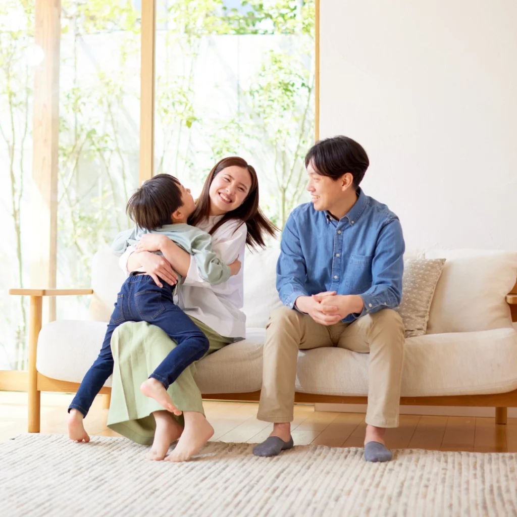 Happy family sitting together in a bright living room, with a child hugging their mother while the father smiles, enjoying a clean and comfortable home environment.